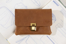 Load image into Gallery viewer, Brown leather wristlet with gold clasp on top of blueprints