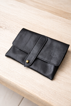 Load image into Gallery viewer, Black leather wallet with a gold button on a light wooden surface